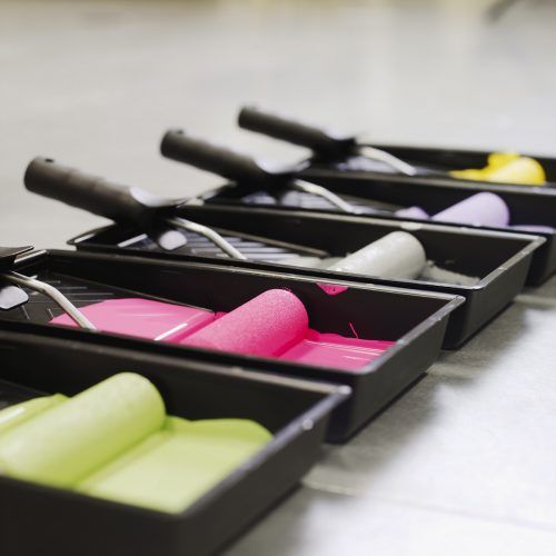Close-up side view of trays of coloured paint and paint rollers